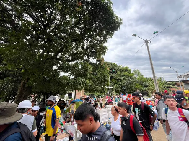 A crowd of evacuated residents gathered under trees in a park in Cali, some carrying bags and water.